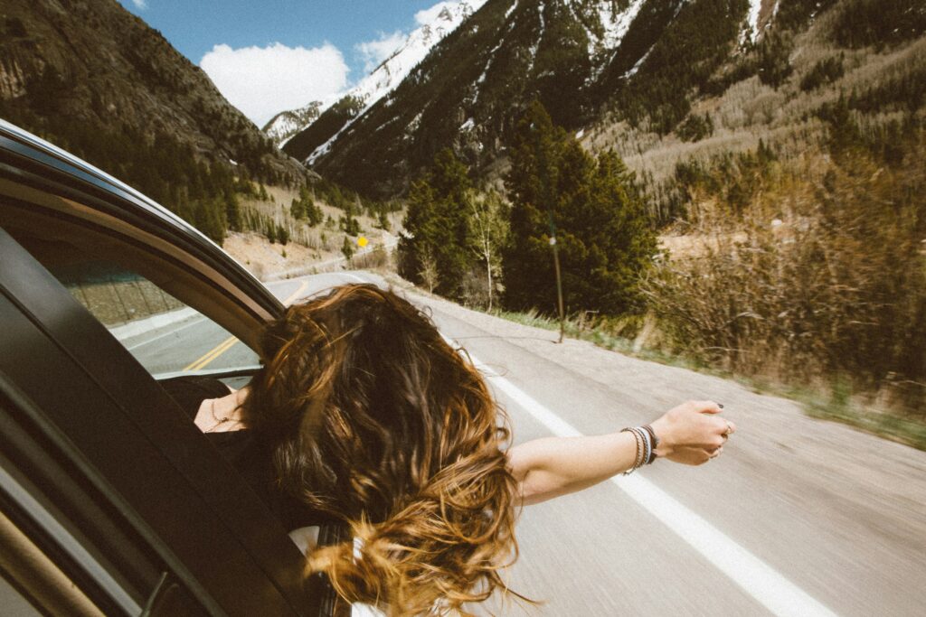 山道を走る車の窓から女性が身を乗り出している風景