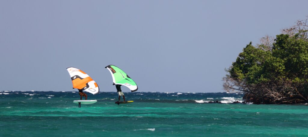 エメラルドグリーンの海の上でカイトサーフィンを楽しむ2人の姿