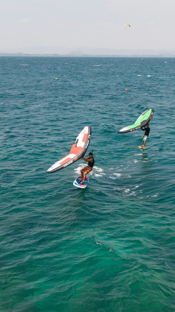 エメラルドグリーンの海の上をサーフボードにのりカイトを楽しむ2人の姿