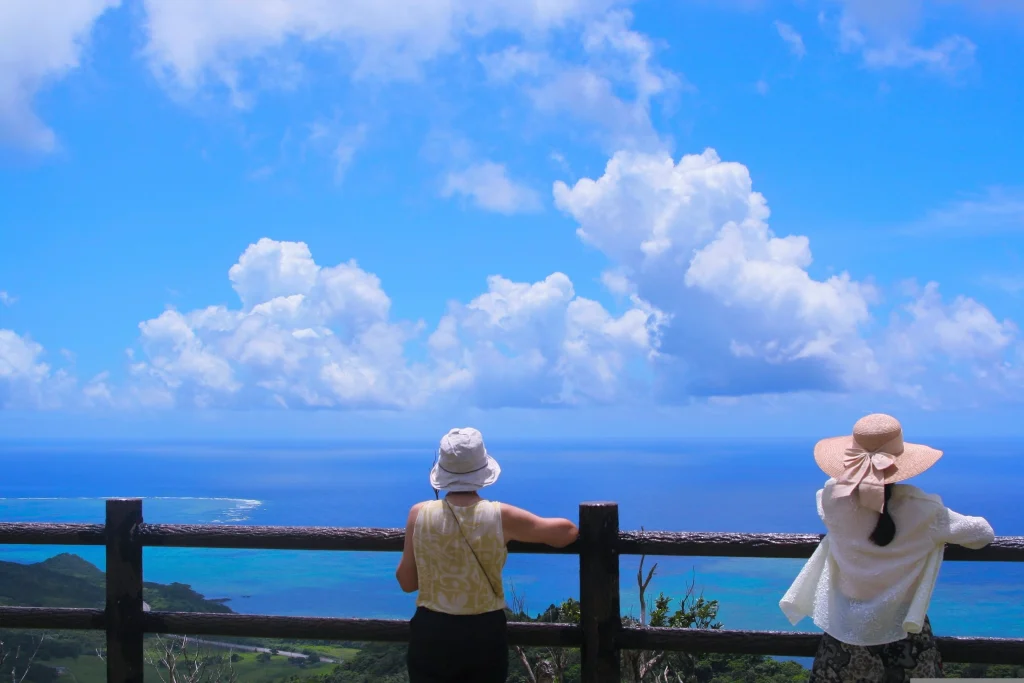 展望台の柵から美しい青い海と空を眺める、帽子をかぶった2人の人物の後ろ姿