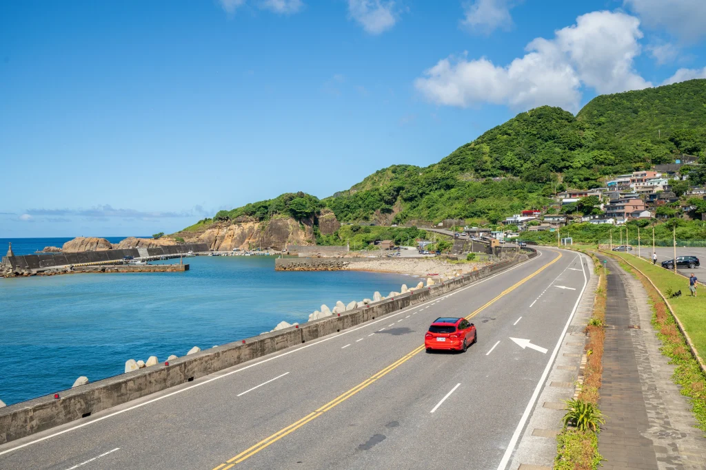 美しい青い海と山に挟まれた海岸沿いの道路を走る赤いレンタカーのドライブ風景